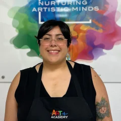 Professional portrait of art teacher with Art Plus Academy logo in the background at Southwest Austin location
