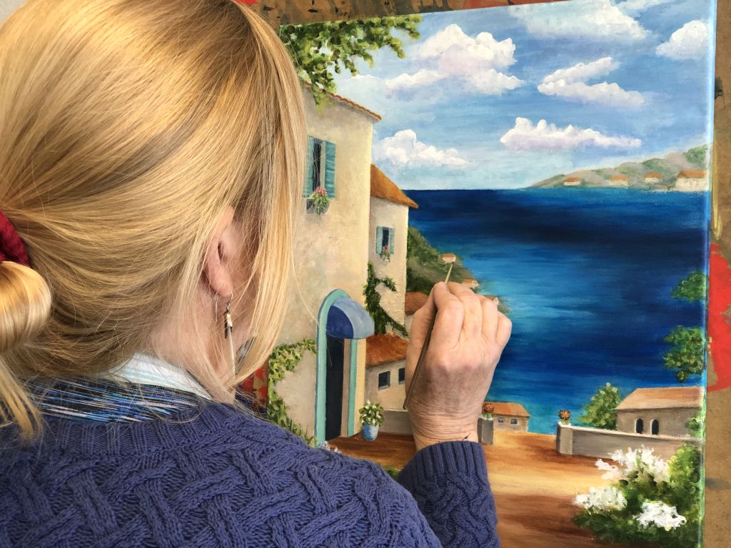 Woman painting a lake landscape with an Italian-style house in the foreground during Art Class in Cedar Park